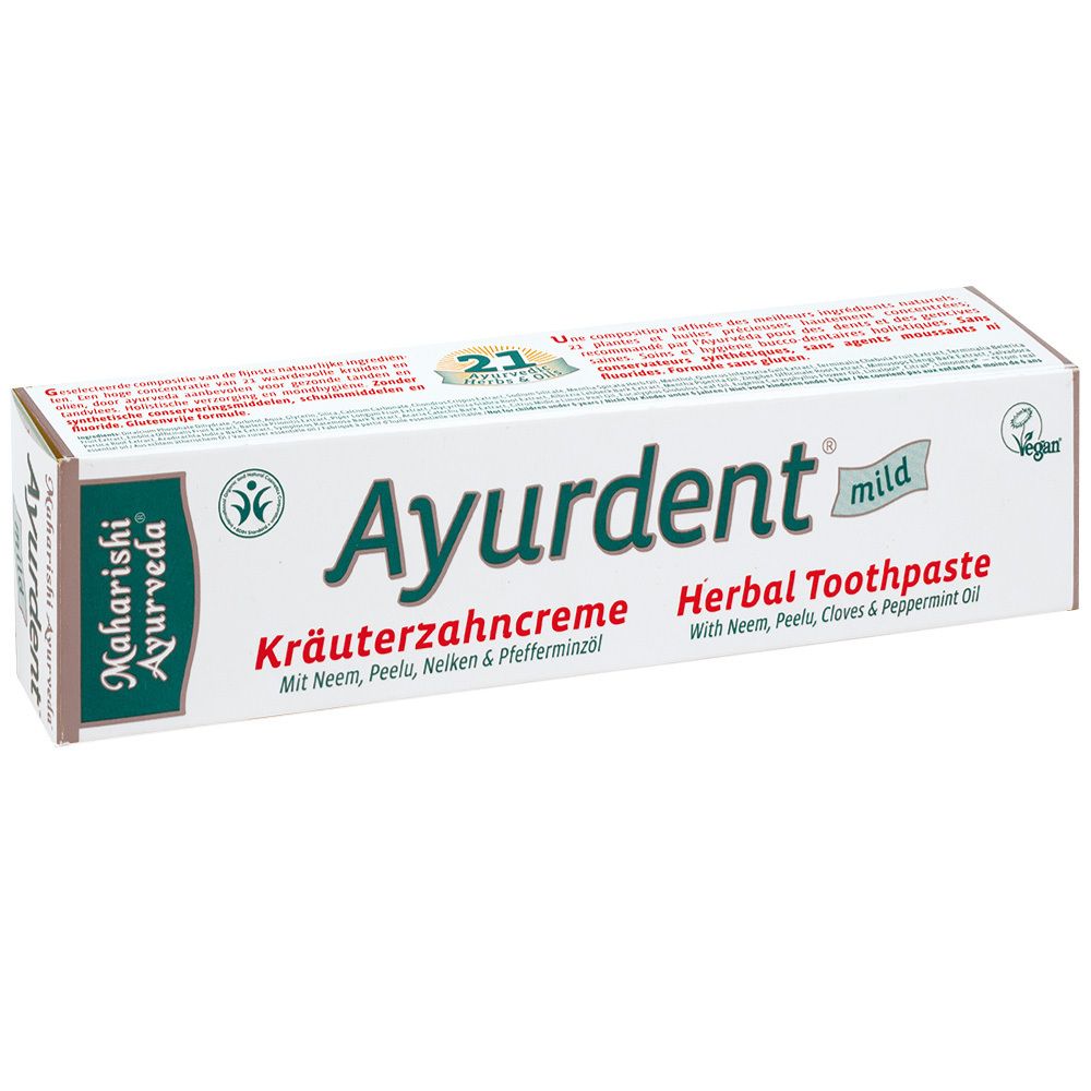 Boîte en carton blanche avec Ayurdent mild Kräuterzahncreme. Logo et texte verts et noirs. Label végétalien.