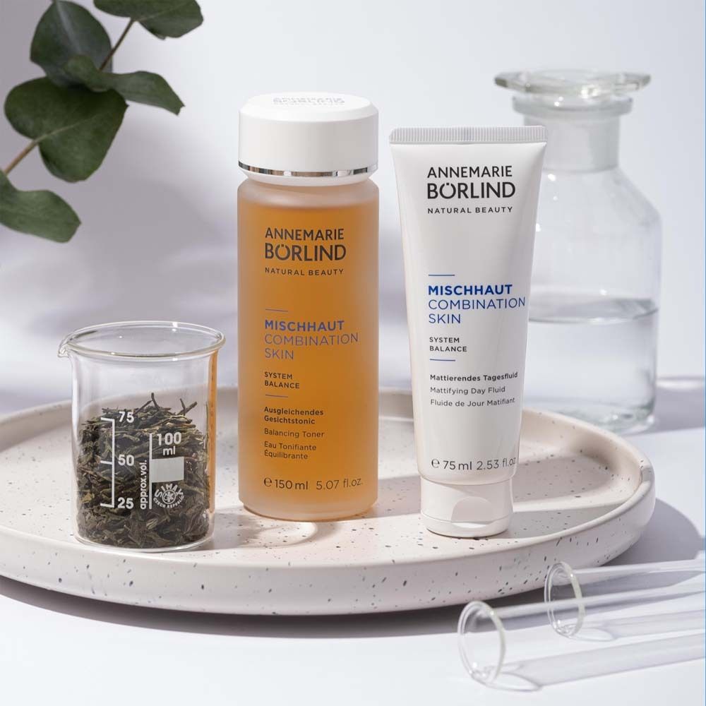 Produits ANNEMARIE BÖRLIND sur plateau. Tonique facial, fluide de jour, bécher avec herbes. Inscription : MISCHHAUT.