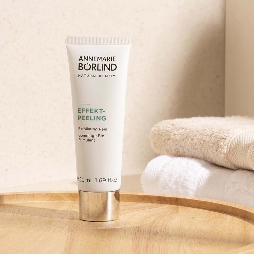 Tube blanc EFFEKT-PEELING d'ANNEMARIE BÖRLIND sur plateau en bois, à côté de serviettes.