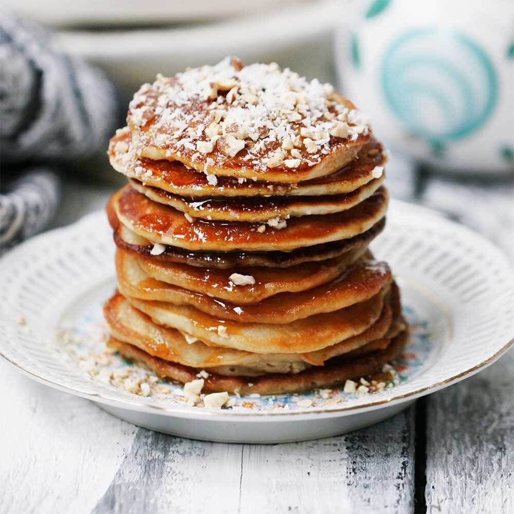 Pile de crêpes sur une assiette, saupoudrées de noix. De petits motifs floraux sont visibles sur l'assiette.