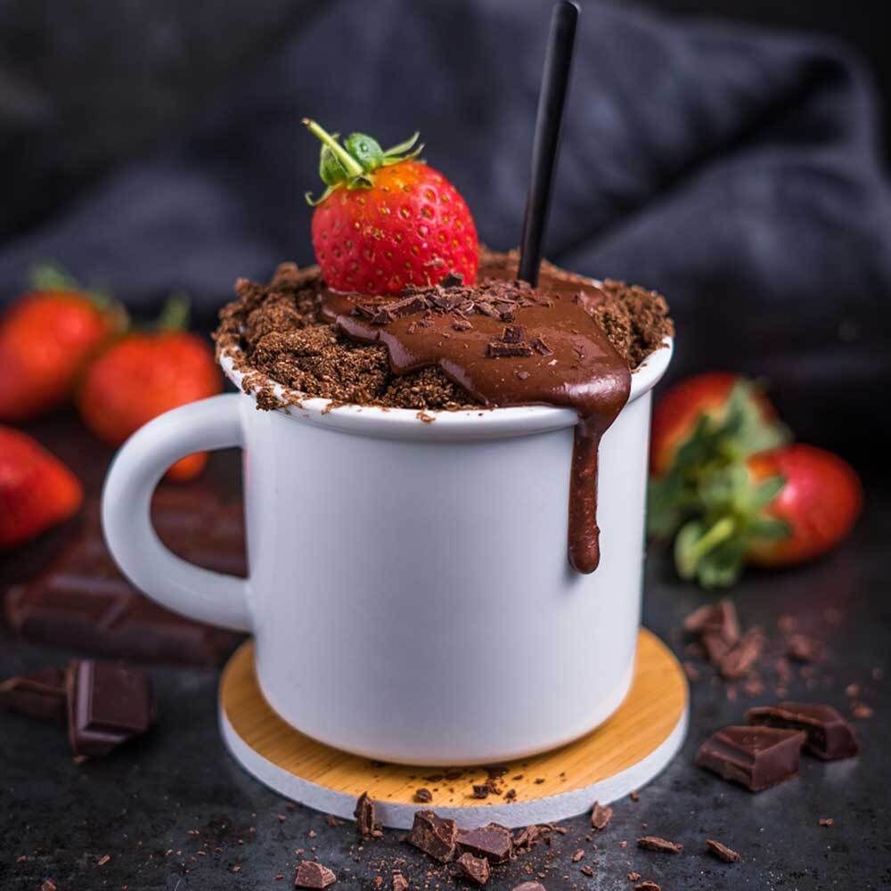 Tasse avec gâteau au chocolat, fraise, morceaux de chocolat. Sur un dessous de verre en bois.