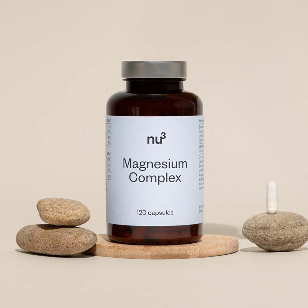 Flacon brun avec étiquette blanche « Magnesium Complex » et « 120 capsules ». Sur une plaque de bois avec des pierres.