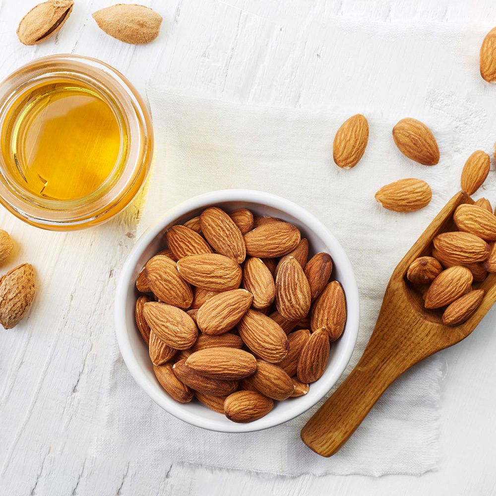 Verre avec huile et bol avec amandes. Pelle en bois avec amandes. Sur fond clair.