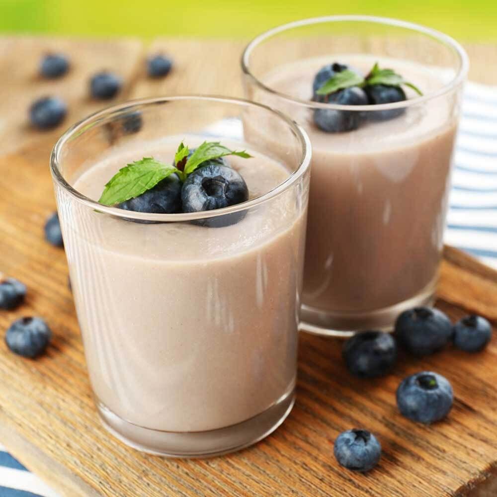 Deux verres de shake violet, myrtilles et menthe sur une planche de bois. Myrtilles éparpillées.