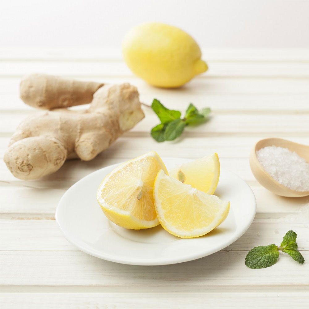 Tranches de citron sur une assiette, gingembre, menthe et sel à côté. Sur fond de bois clair.