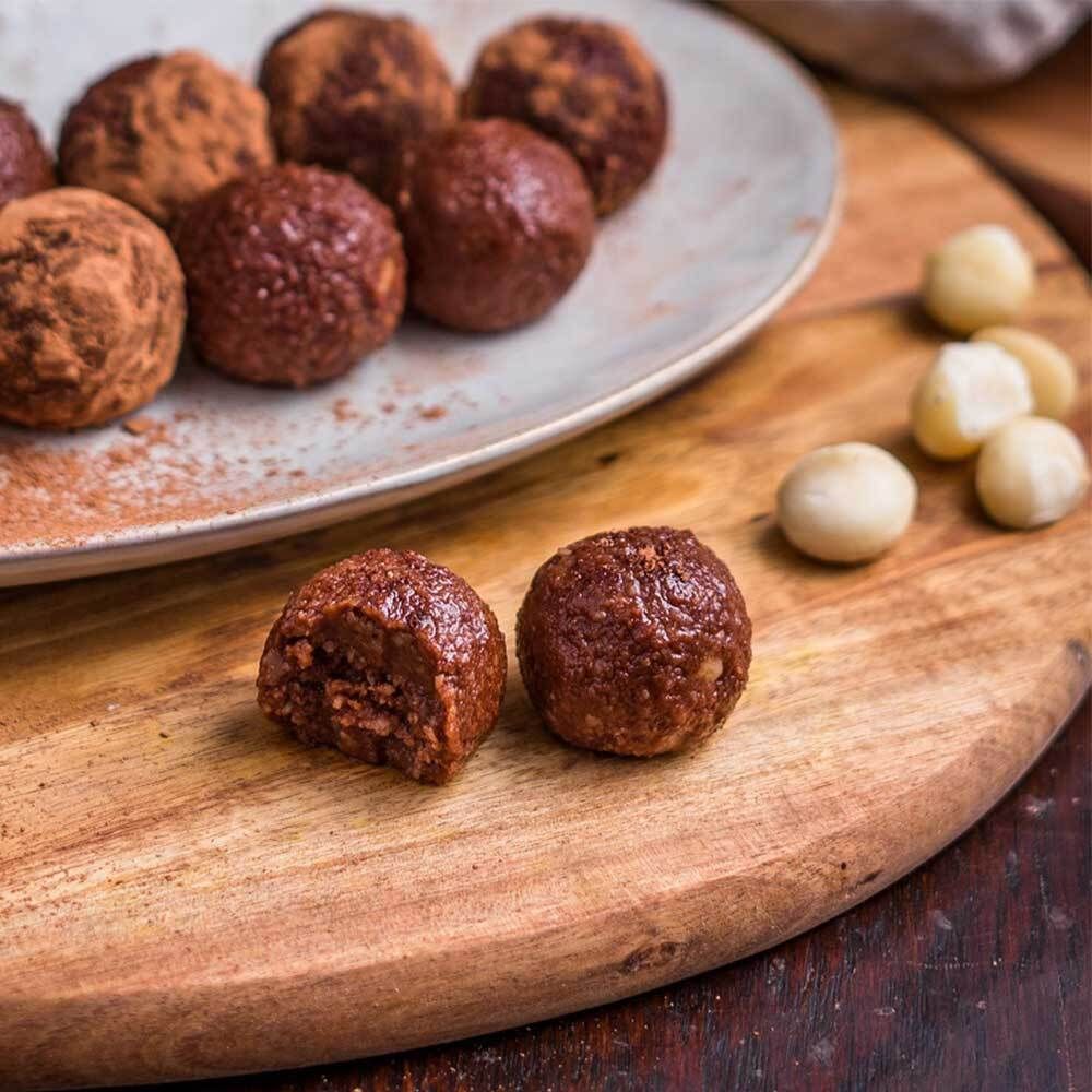 Boules de cacao sur planche de bois. Certaines boules sont coupées, avec des noix de macadamia.
