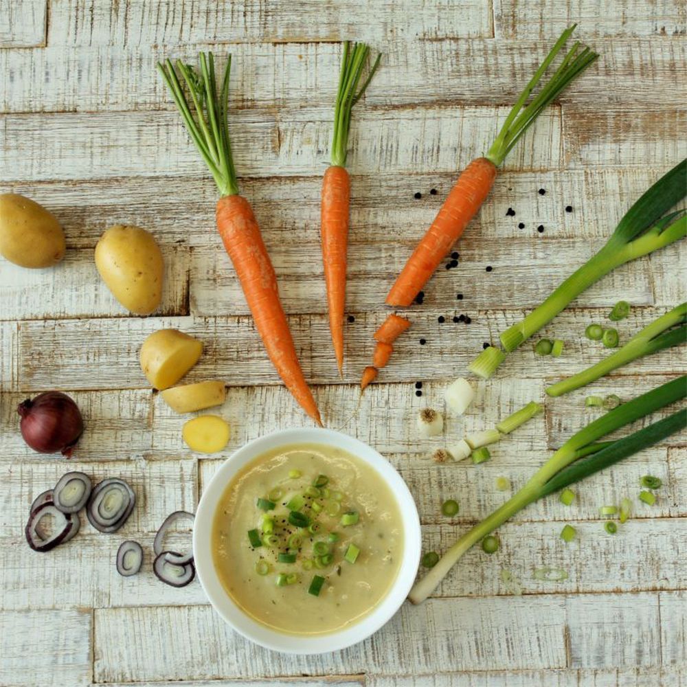 Bol de soupe de pommes de terre avec oignons verts. Carottes, pommes de terre, oignons, grains de poivre et poireaux sur planche.