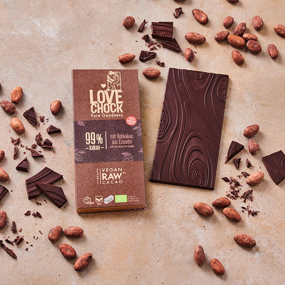Tablette LOVECHOCK 99% cacao à côté de l'emballage ouvert. Fèves de cacao et morceaux de chocolat éparpillés.
