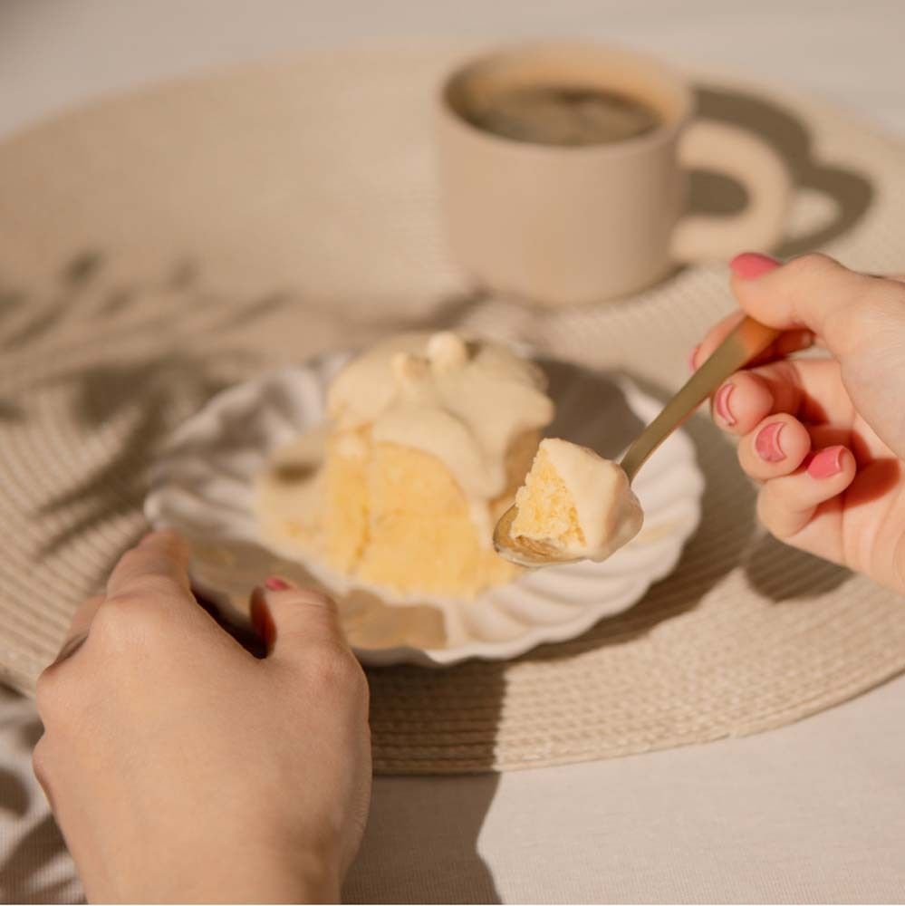 Personne tenant une cuillère avec glaçage au beurre d'amandes au-dessus d'un morceau de gâteau. Tasse de café et serviette sur la table.