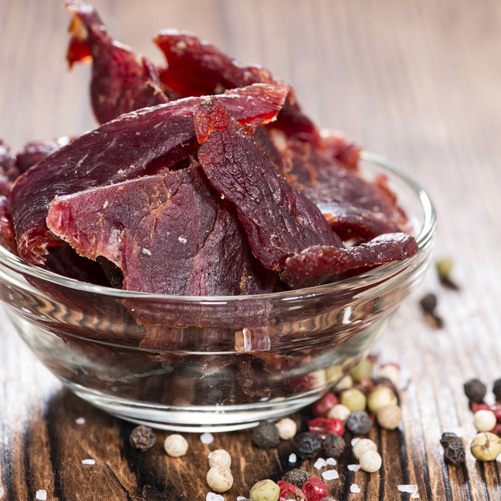 Bol en verre avec du Beef Jerky. Sur une table en bois. Graines de poivre et sel à côté.