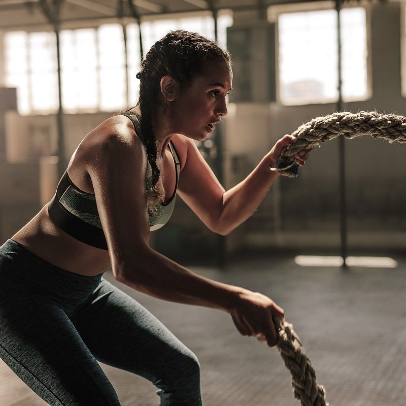 Une femme s'entraîne avec une corde dans une salle de sport. Elle porte des vêtements de sport.