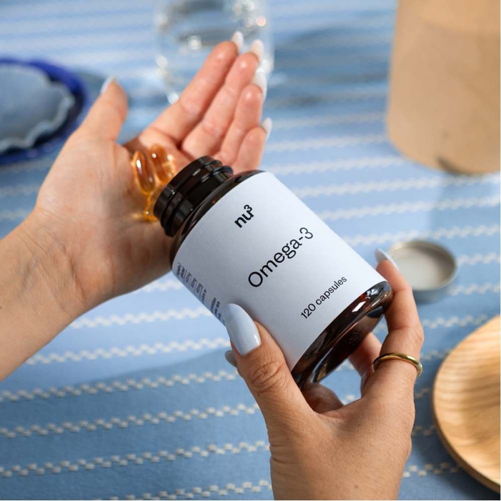 Personne tenant une bouteille de nu3 Omega-3 et des gélules. Bouteille marron, étiquette blanche.