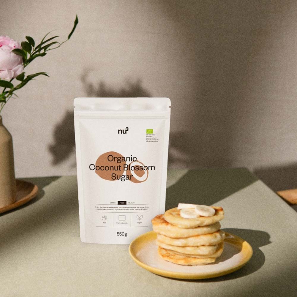 Un paquet de nu3 Organic Coconut Blossom Sugar à côté d'une assiette de crêpes avec des tranches de banane.