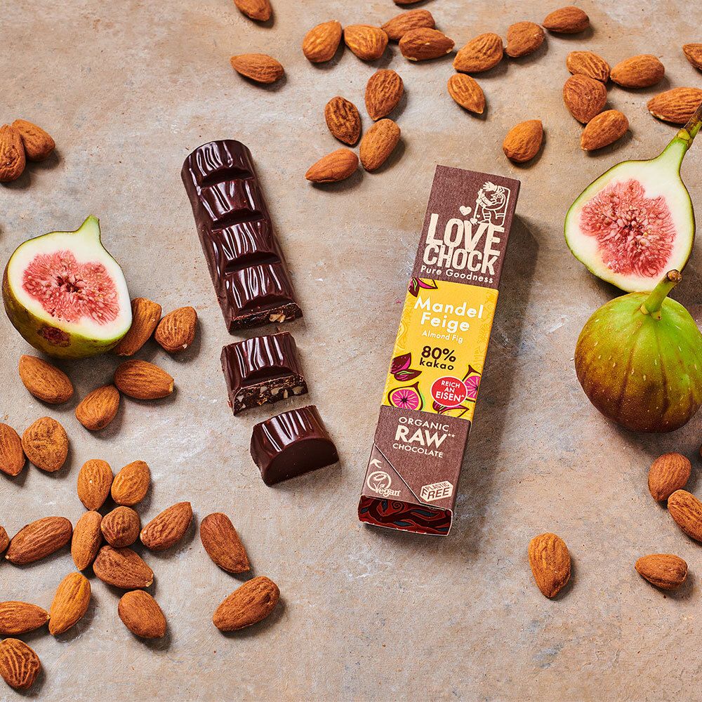 LOVECHOCK Mandel-Feige 80% Kakao, partiellement cassé. Amandes et moitiés de figues à côté. Emballage visible.