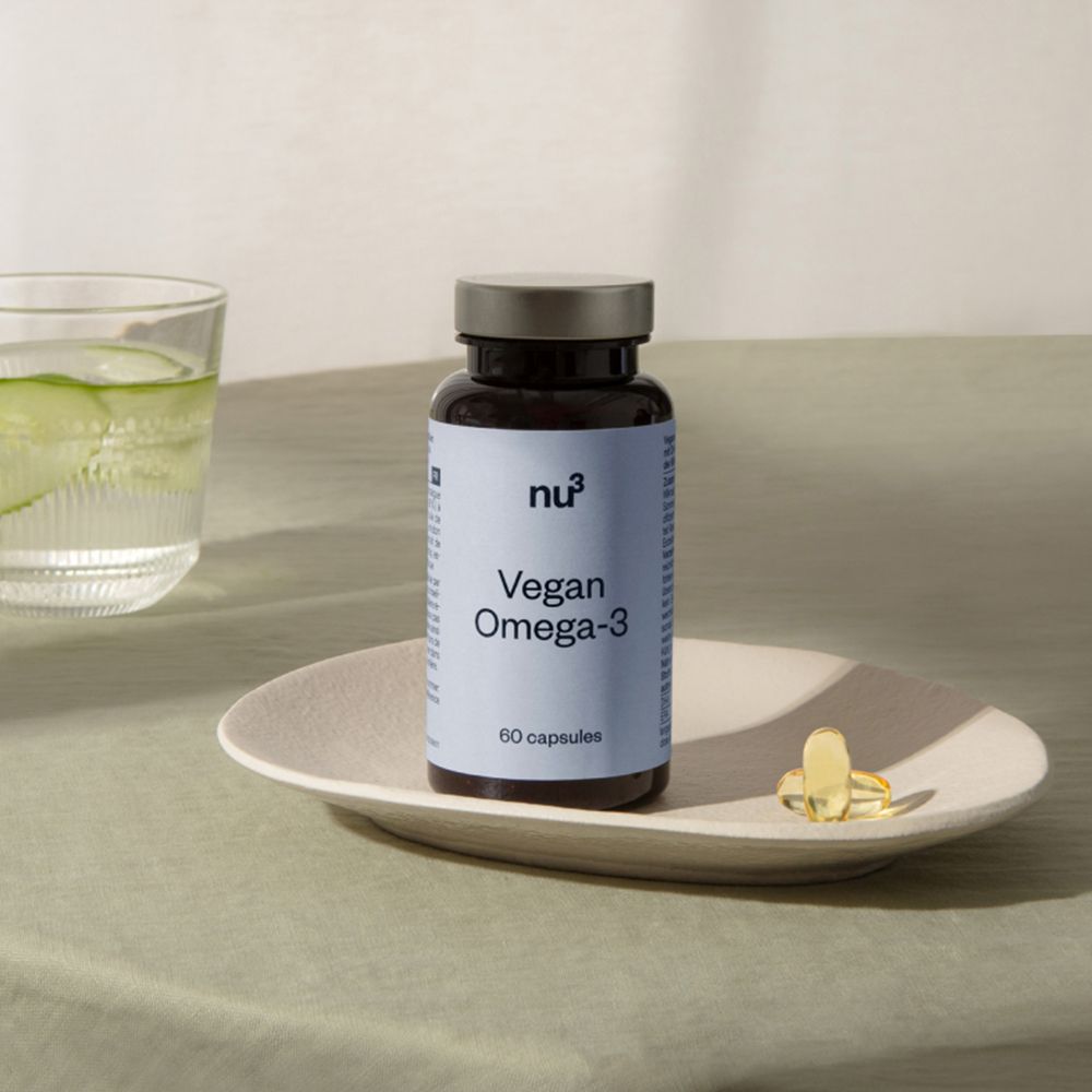 Un flacon "nu3 Vegan Omega-3" sur une assiette avec une gélule et un verre d'eau.