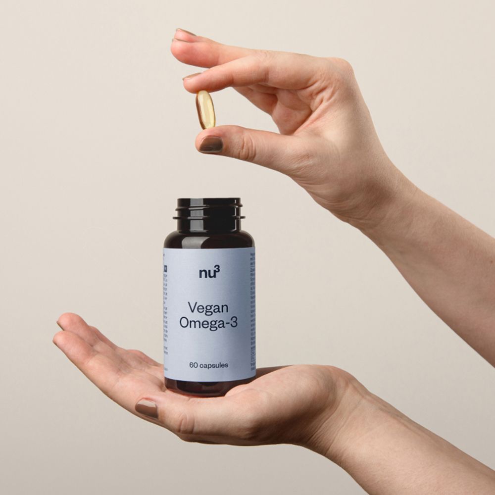 Mains tenant une gélule au-dessus d'un flacon "nu3 Vegan Omega-3".
