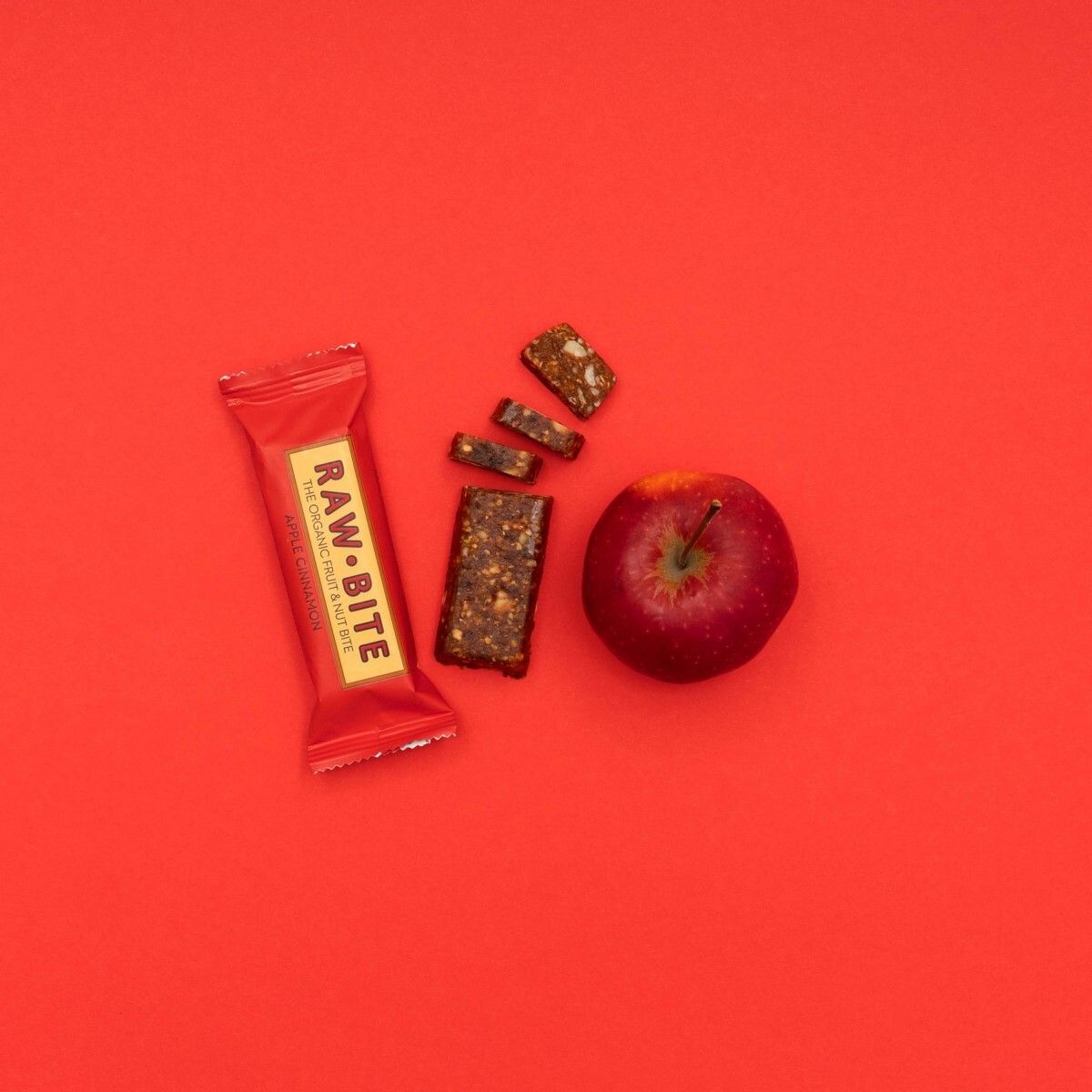 Surface rouge avec barre, morceaux de barre et pomme. Inscription RAWBITE visible.