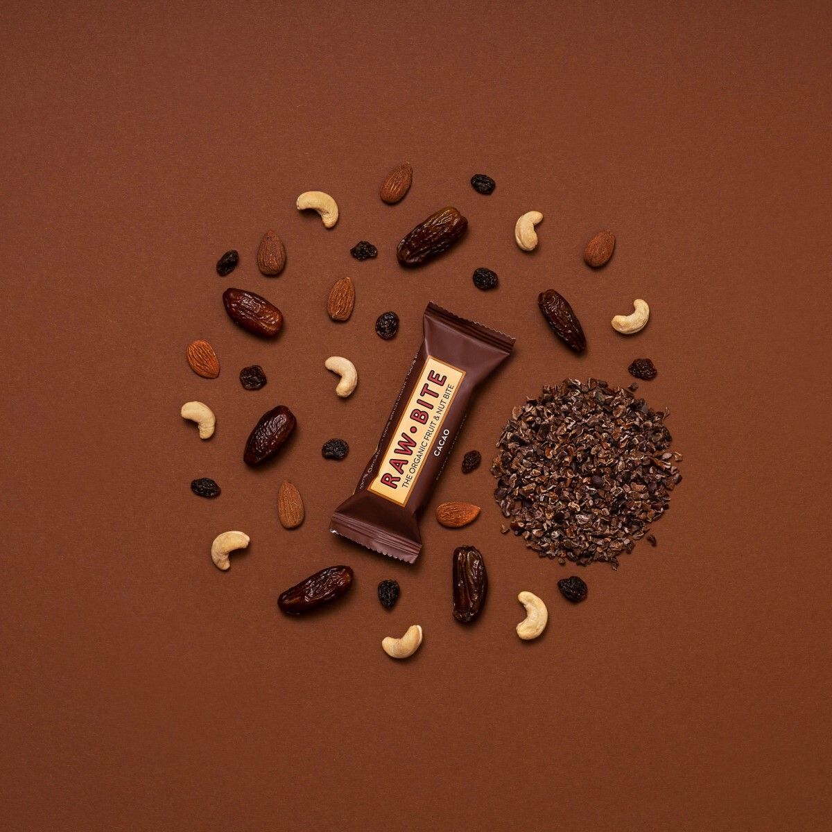 Barre entourée de noix, cacao et fruits secs. Inscription : RAWBITE, THE ORGANIC FRUIT & NUT BITE, CACAO.