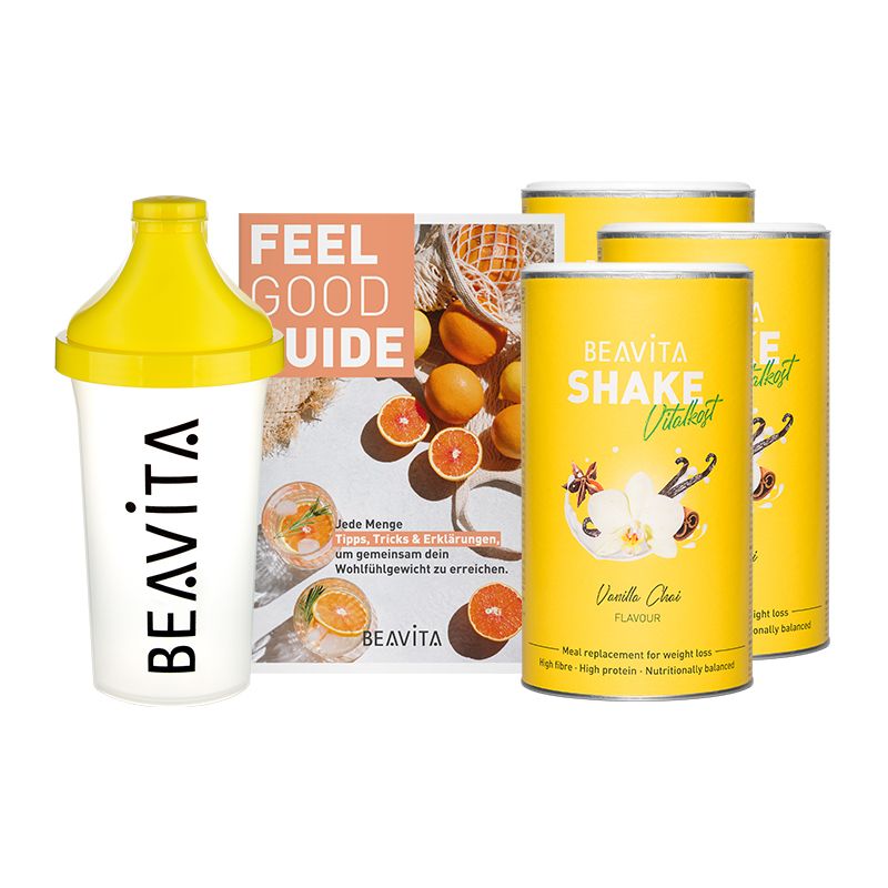 Pack de régime avec shaker, brochure et boîtes. Boîtes avec "BEAVITA Shake Vital+kost Vanilla Chai". Shaker jaune et blanc. Brochure avec fruits.