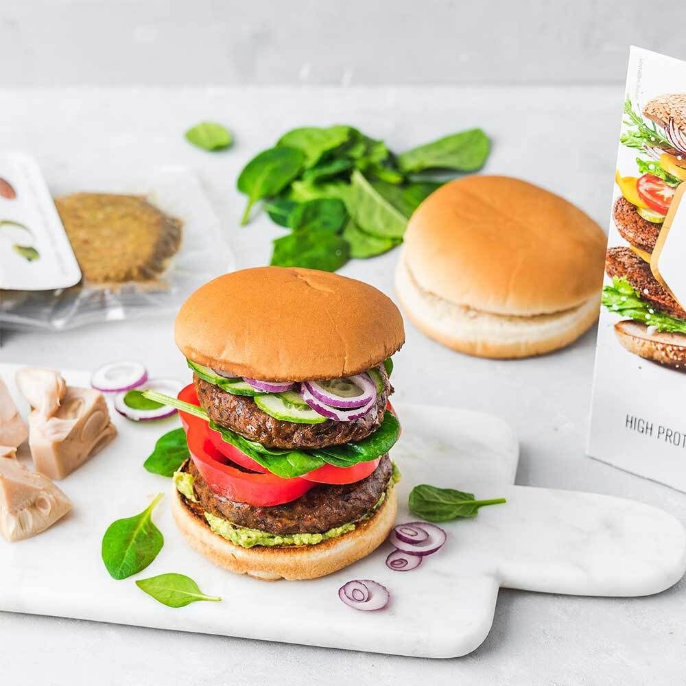 Burger avec ingrédients sur une planche. Contient des burgers, des petits pains, des tomates, des concombres, des oignons et des épinards.