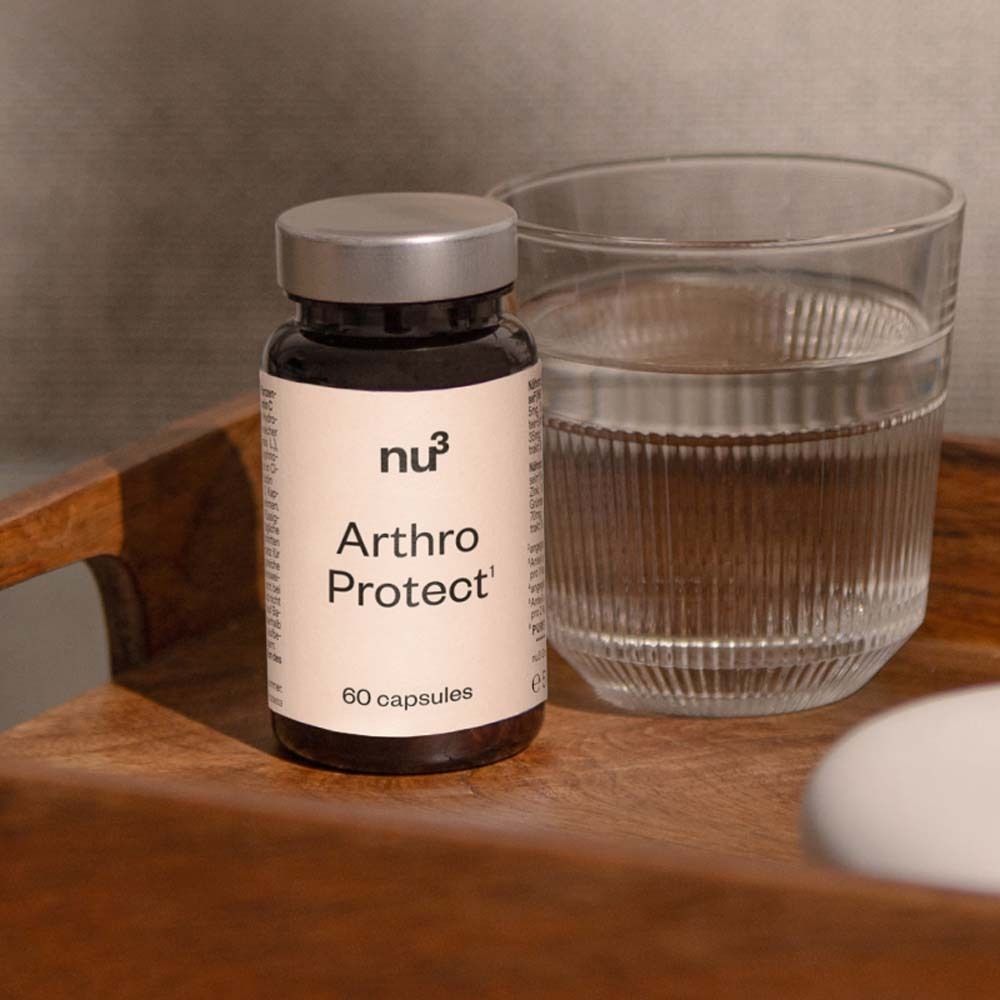 Flacon brun avec couvercle argenté. Inscription : Arthro Protect, logo nu3. 60 gélules. À côté du flacon : verre d'eau, plateau en bois.