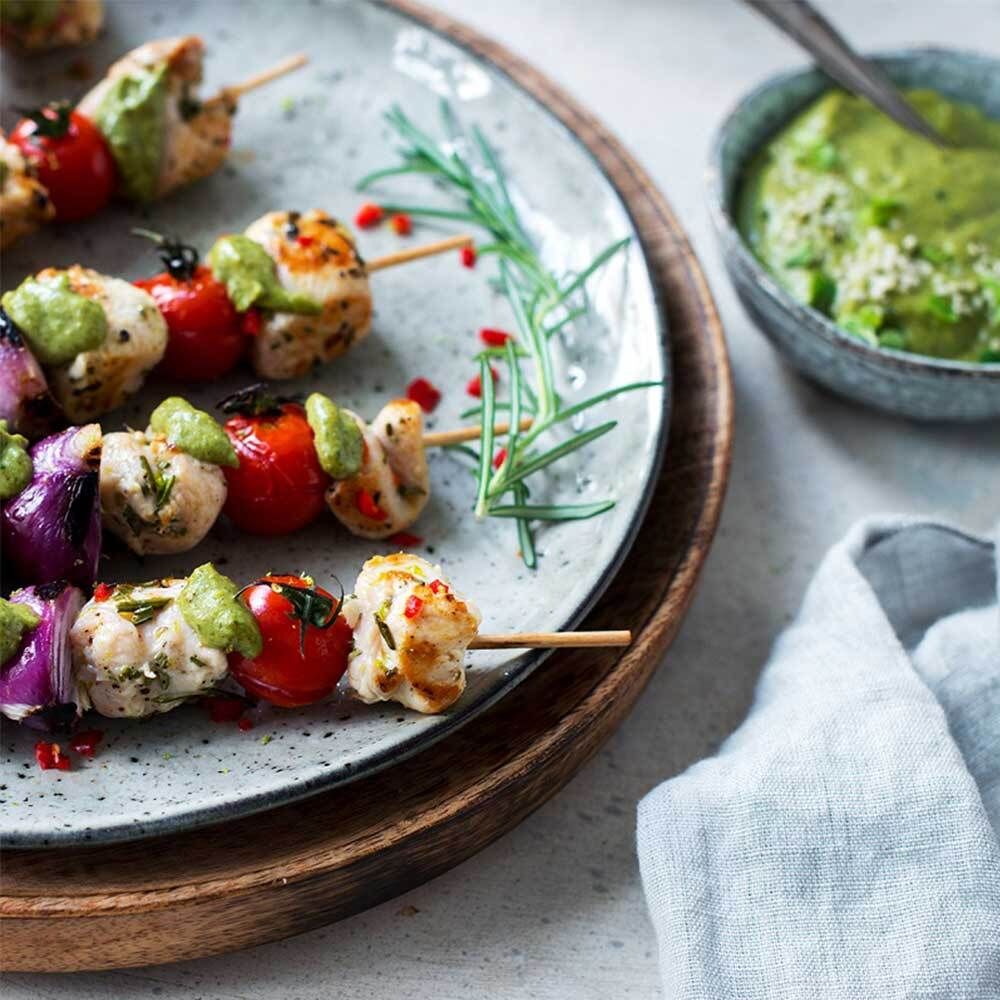 Assiette avec brochettes de tomates, oignons et poulet. Sauce verte dans un bol. Branche de romarin.