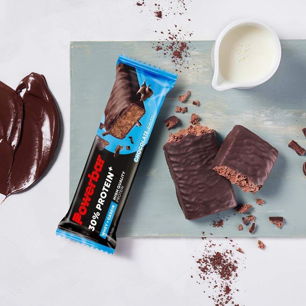 Barre PowerBar 30% Protein Plus Chocolate et morceaux cassés. Sur planche de bois avec lait. Sauce au chocolat.