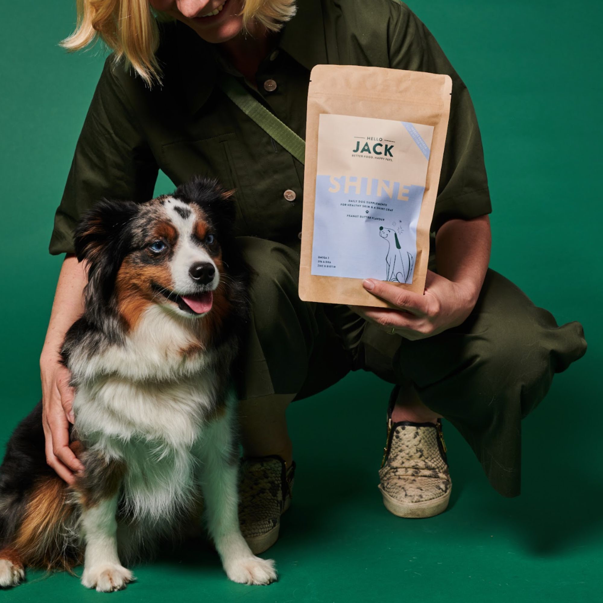 Femme tenant un sachet "Hello Jack Shine" à côté d'un chien. Le chien est assis. Saveur beurre de cacahuète.