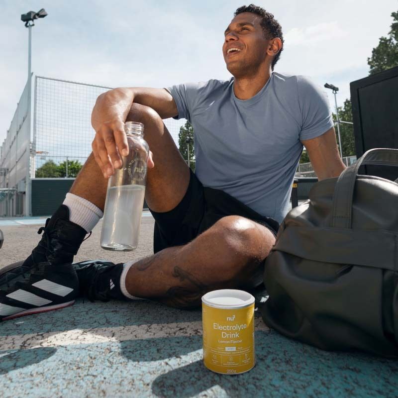 Homme assis après le sport à côté de la boîte Nu3 Elektrolyte Drink et d'une bouteille d'eau.
