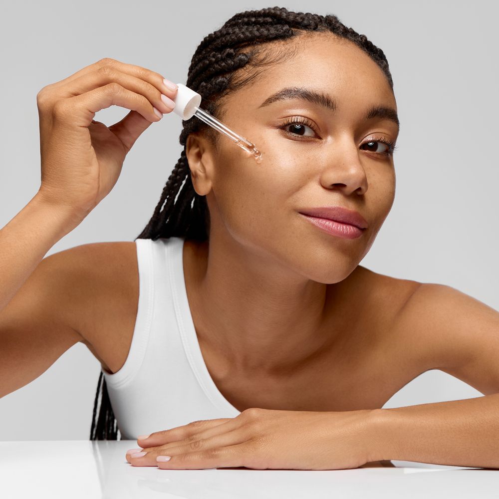 Une femme applique un sérum sur son visage à l'aide d'un applicateur à pipette.