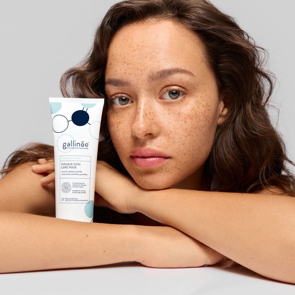 Une femme tient un tube blanc de masque pour le visage Gallinée. Le tube a un design bleu et blanc.