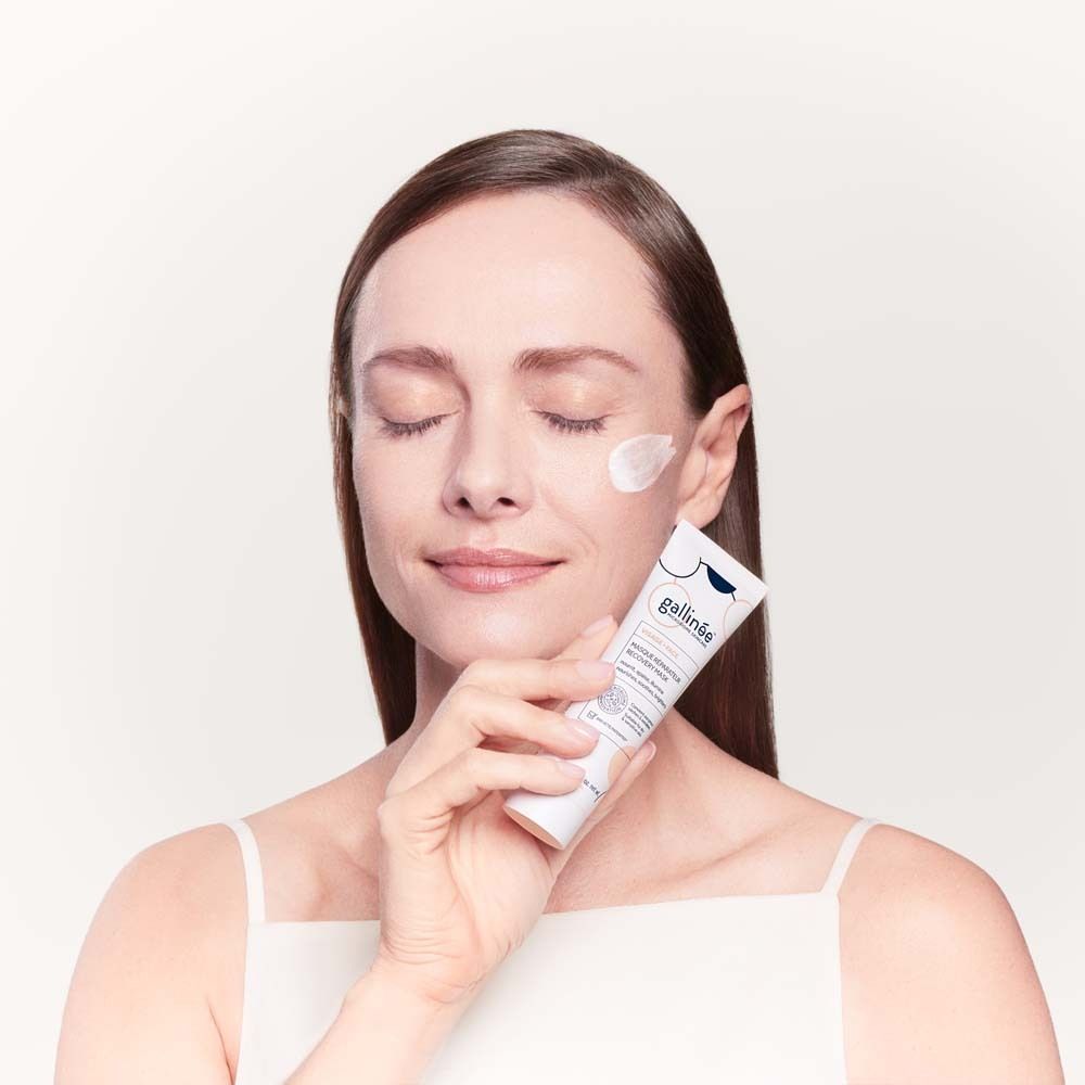 Femme aux yeux fermés tenant un tube gallinée™ Face Recovery Mask. Crème sur la joue.