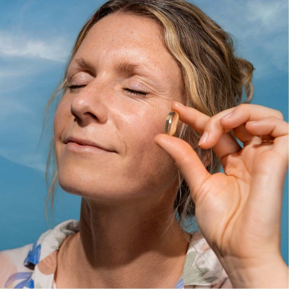Femme tenant une gélule dorée entre les doigts. Elle ferme les yeux.