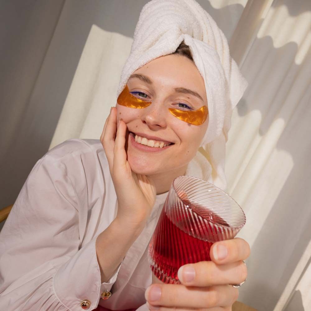 Femme avec patchs pour les yeux tenant un verre de boisson rouge. Une boîte en arrière-plan.