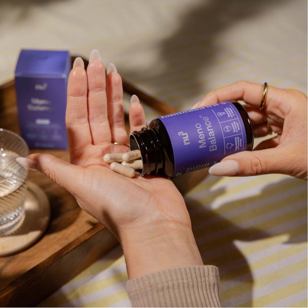 Mains tenant des gélules d'un flacon. Marque: nu3 Meno Balance. Étiquette violette.