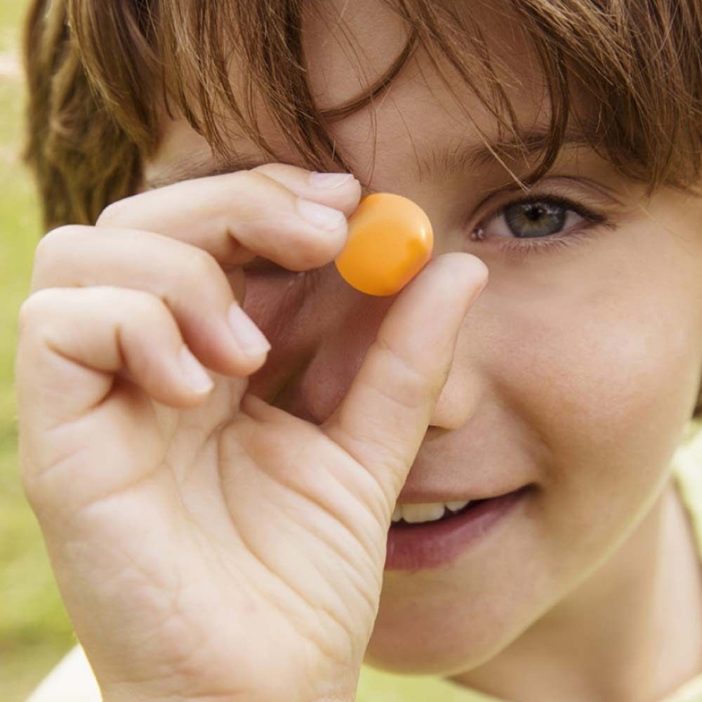 Un enfant tient un bonbon gélifié oméga-3 orange devant son œil. L'enfant sourit.