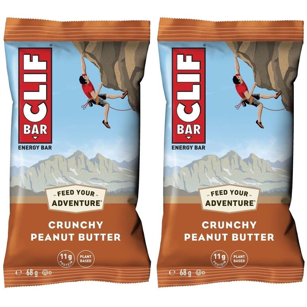 Deux barres énergétiques CLIF Bar Crunchy Peanut Butter. Emballage avec illustration d'alpiniste. Texte : "Crunchy Peanut Butter", "11g Protein", "Plant Based".
