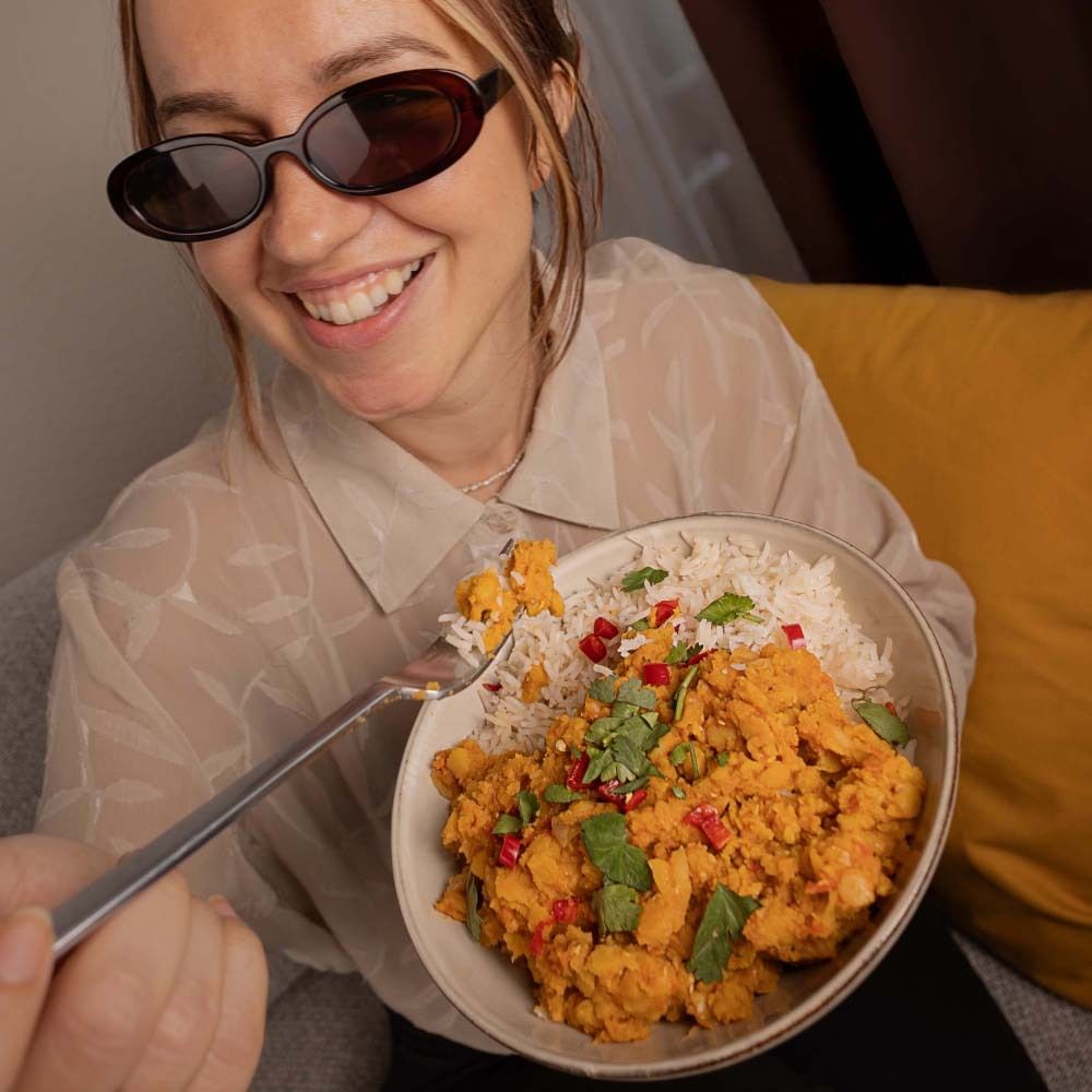 Personne mange du nu3 Organic Lentil Curry avec du riz dans un bol. Lunettes de soleil.