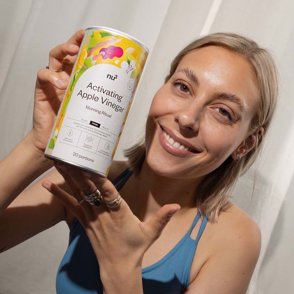 Femme tenant une boîte "Activatin Apple Vinegar". Logo "nu3" et texte "Morning Ritual" visibles. La femme sourit.