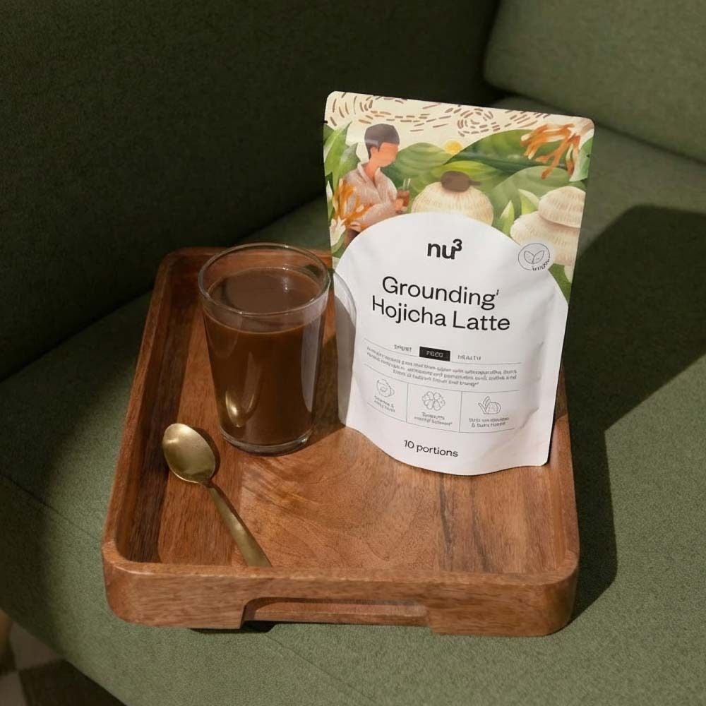 Plateau en bois avec verre de boisson, emballage du produit nu3 Grounding Hojicha Latte et cuillère dorée.