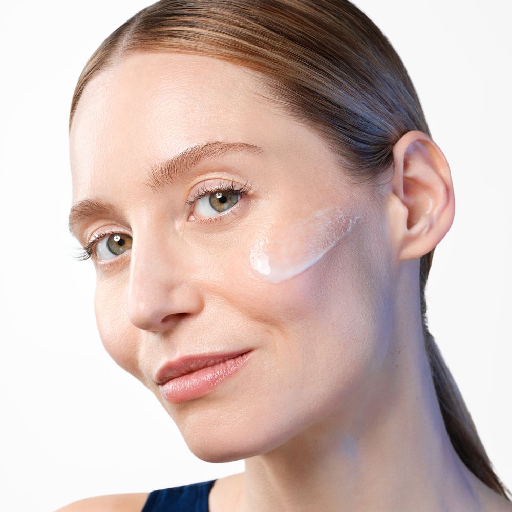Femme avec crème sur la joue. Peau claire, cheveux bruns. Regard caméra.