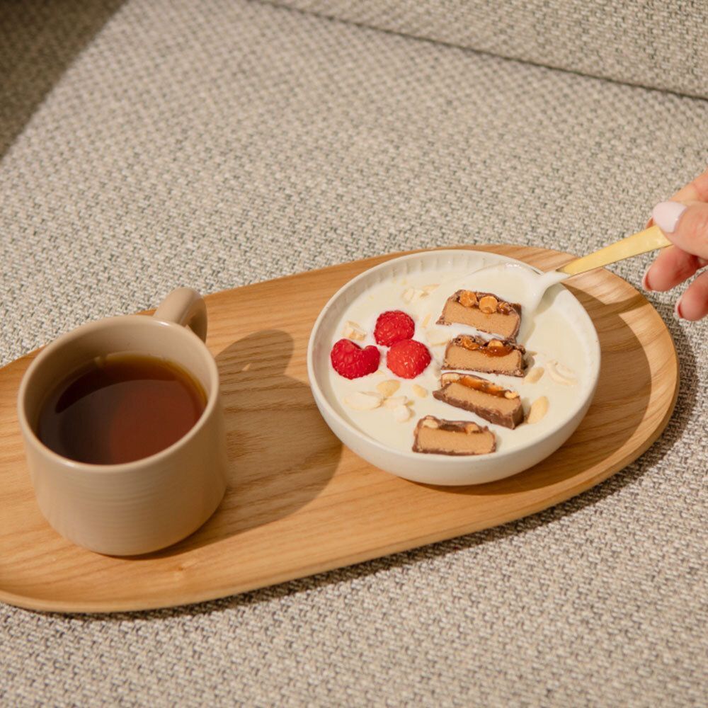 Barres nu3 Fit Protein coupées en morceaux dans un bol avec du yaourt, des baies et des éclats d'amande, à côté d'une tasse de thé.