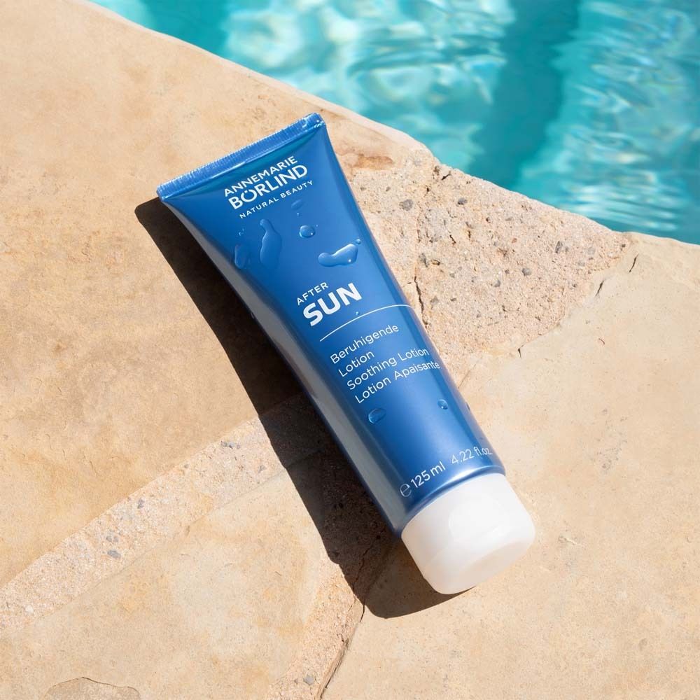 Tube bleu avec bouchon blanc au bord de la piscine. Inscription : AFTER SUN, Lotion apaisante. Eau en arrière-plan.