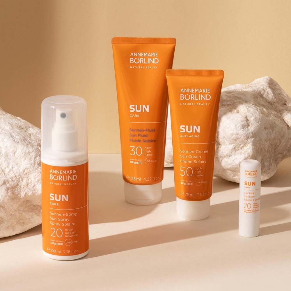 Quatre produits de protection solaire. Spray, fluide solaire, crème solaire et soin des lèvres. Orange et blanc. Inscription : SUN.