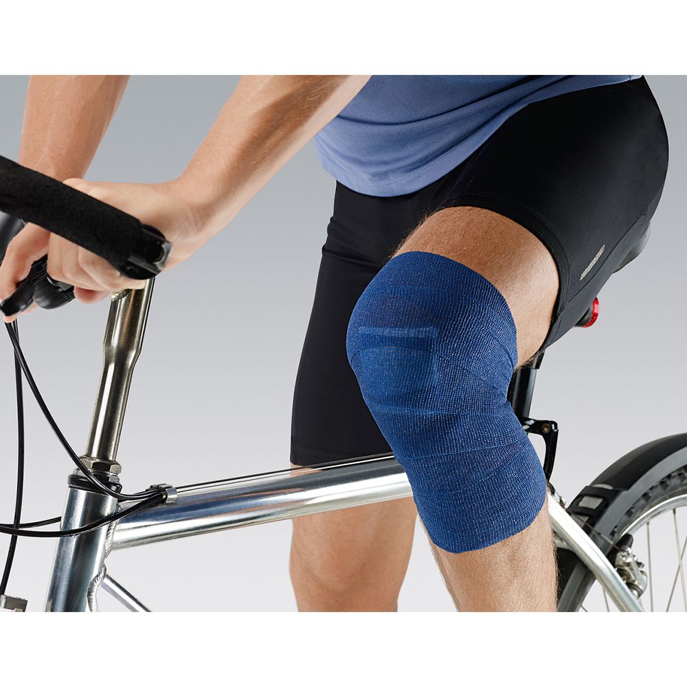 Personne à vélo avec bandage Peha-haft® Color bleu sur le genou. Le bandage recouvre le genou.