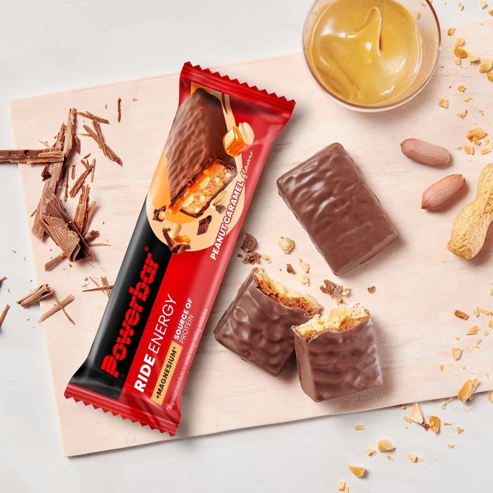 Barre PowerBar Ride Energy. Cacahuète caramel. Sur planche de bois. Barres ouvertes et ingrédients. Vue de dessus.