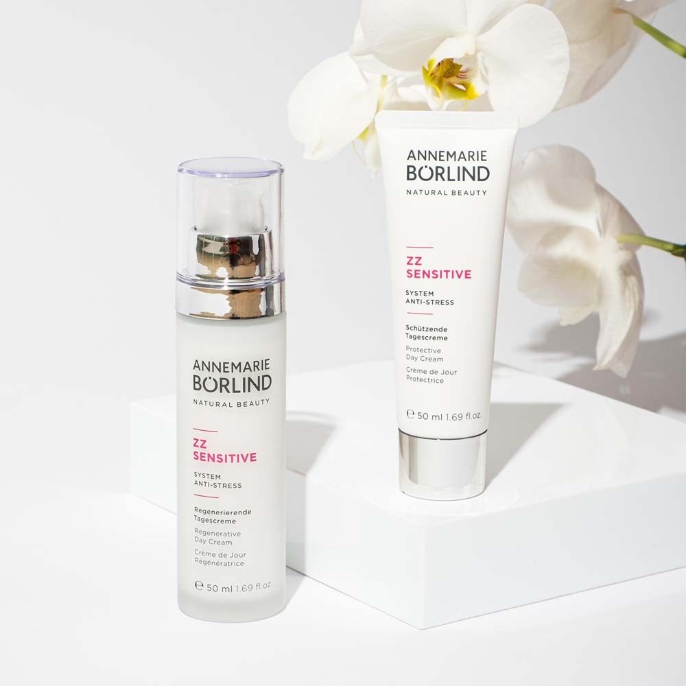 Deux produits: flacon de crème et tube. Inscription: ANNEMARIE BÖRLIND, ZZ SENSITIVE. Surface blanche avec orchidées.