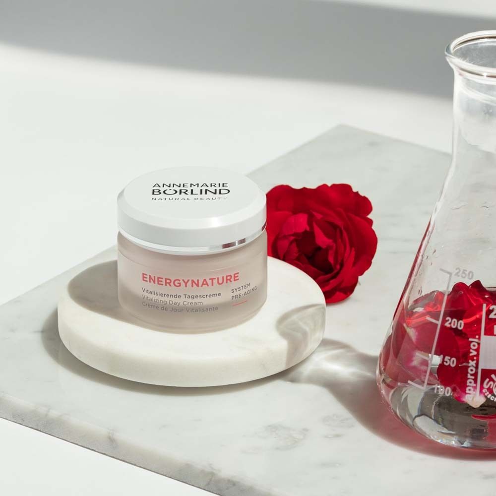 Pot de crème à côté d'une rose et d'un récipient en verre. Inscription ENERGYNATURE, Crème de Jour Vitalisante.