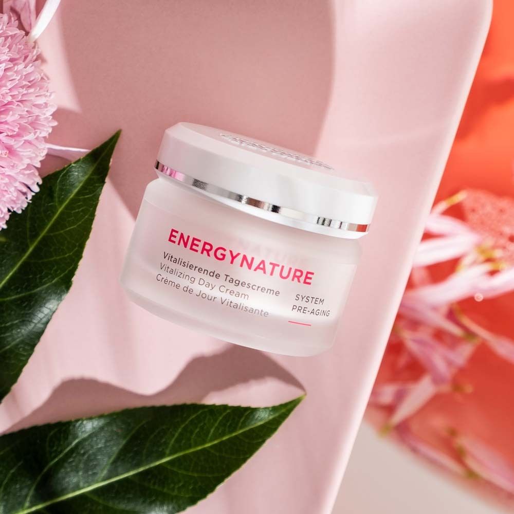 Pot de crème avec inscription ENERGYNATURE, Crème de Jour Vitalisante. Sur fond rose avec des feuilles.