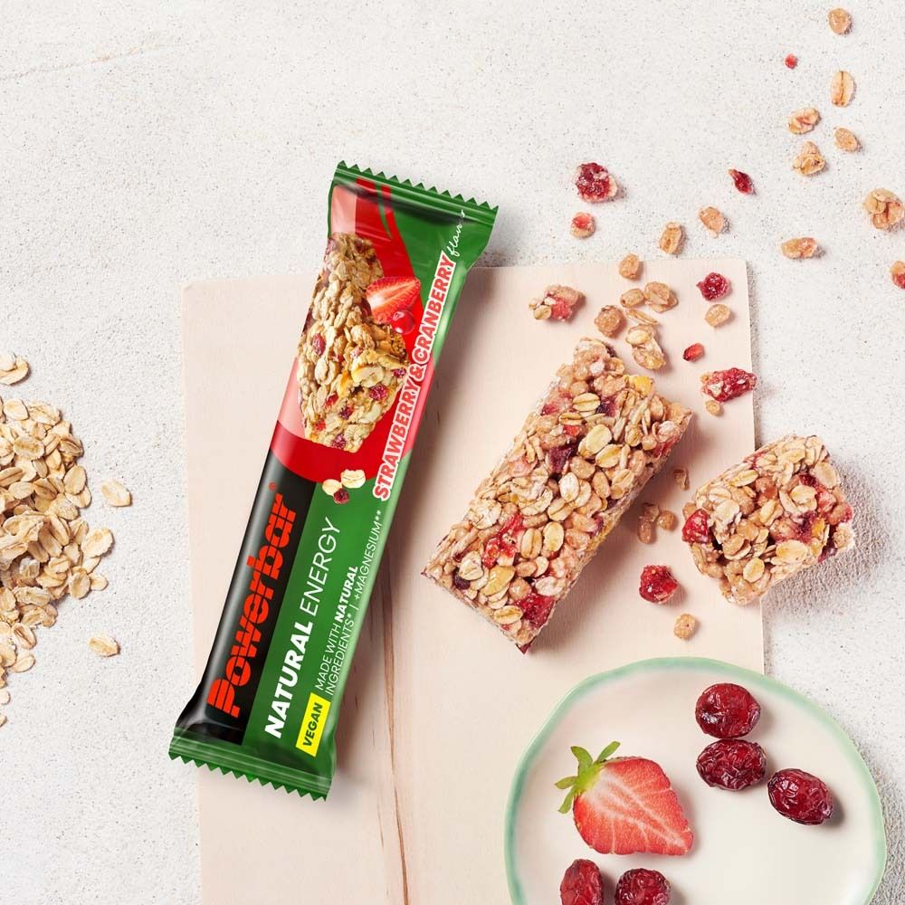Barre Powerbar Natural Energy fraise-canneberge, partiellement consommée, avec fruits et muesli sur support.